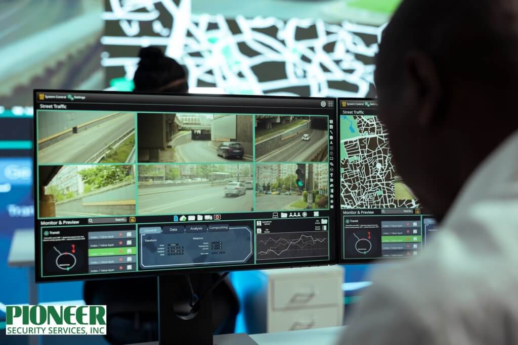 A person sits in a control room, viewing multiple video feeds of street traffic and a digital map on a large, multi-screen computer monitor. The screen displays video from several traffic cameras, along with data analysis and system controls.