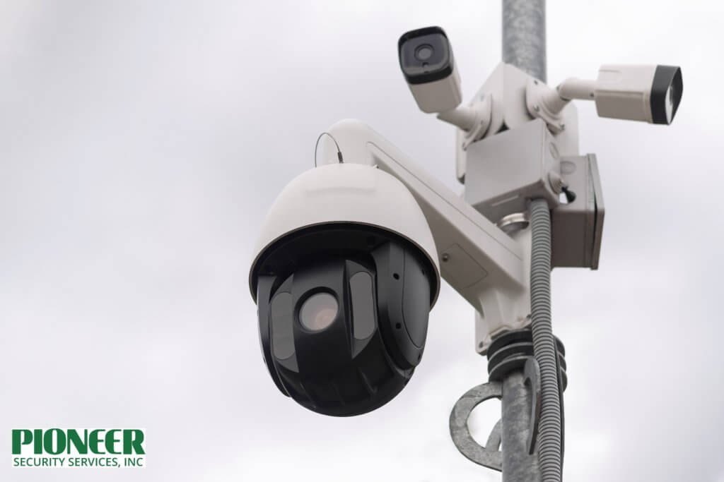 A close-up, low-angle shot of a multi-camera traffic monitoring system mounted on a pole against an overcast sky. It features a large, black, dome-shaped PTZ (Pan-Tilt-Zoom) camera and two smaller, white bullet-style cameras.