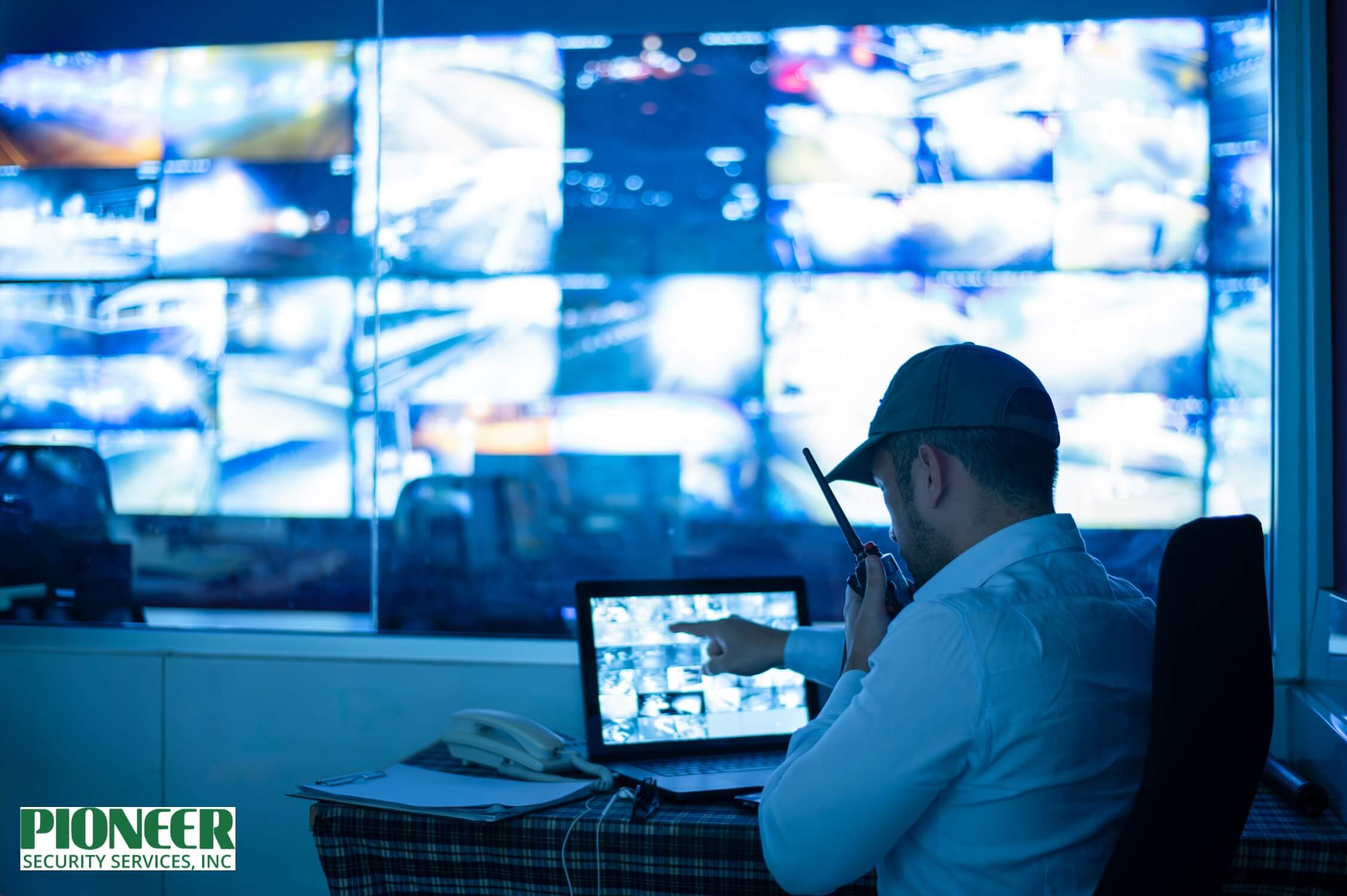 A side view of a focused security monitoring specialist wearing a headset in a dark room illuminated by orange backlighting. He is surrounded by multiple monitors displaying a grid of surveillance video feeds from interior hallways and stairwells, along with technical data.